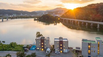 Un hotel a la orilla del río con arquitectura moderna, un puente al fondo y un atardecer.