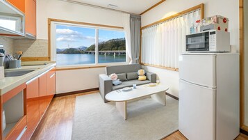 A compact kitchen with a view of a bridge and water, a sofa with cushions, a microwave, and a refrigerator.