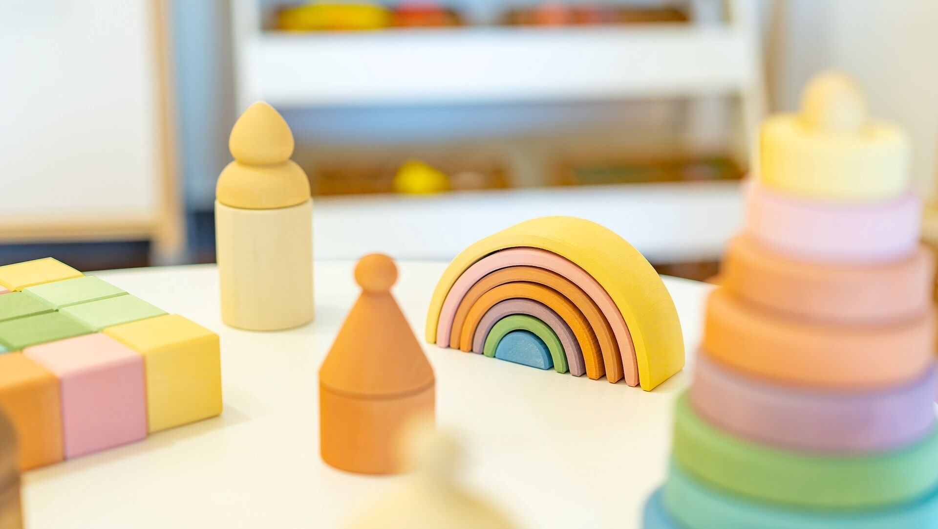Zona de juegos para niños con varios juguetes, incluyendo un juguete de apilar en forma de arcoíris, un juguete piramidal pequeño y un juego de bloques de colores.