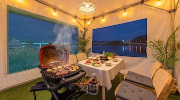 Un área de comedor al aire libre con carpa, una parrilla, mesa servida con comida y vistas a un cuerpo de agua.