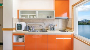 A compact kitchen with orange cabinets, a microwave, a kettle, and a sink. - Chuncheon El Dorado Kid's Pension (Chuncheon)
