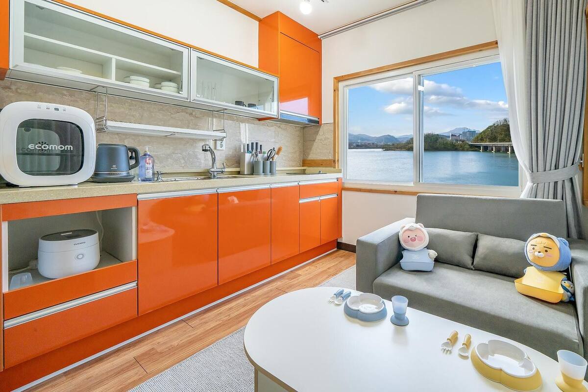 A modern kitchen with orange cabinets, a built-in microwave, and a window with a view of a lake.