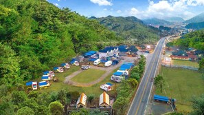 An aerial view of a campsite with RVs and tents, a main building with a blue roof, and a road leading through the area.