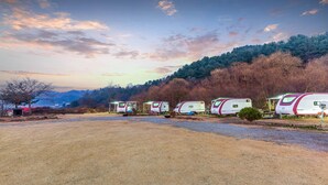 A row of RVs parked in a campground with a forested hillside in the background. - Gapeyong Unak Holiday Caravan (Gapyeong)