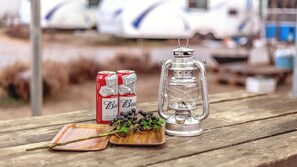 A wooden table with a metal lantern, two cans of Budweiser, and a branch with berries.