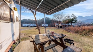 A covered outdoor area with a picnic table, a lantern, and camping equipment. - Gapeyong Unak Holiday Caravan (Gapyeong)