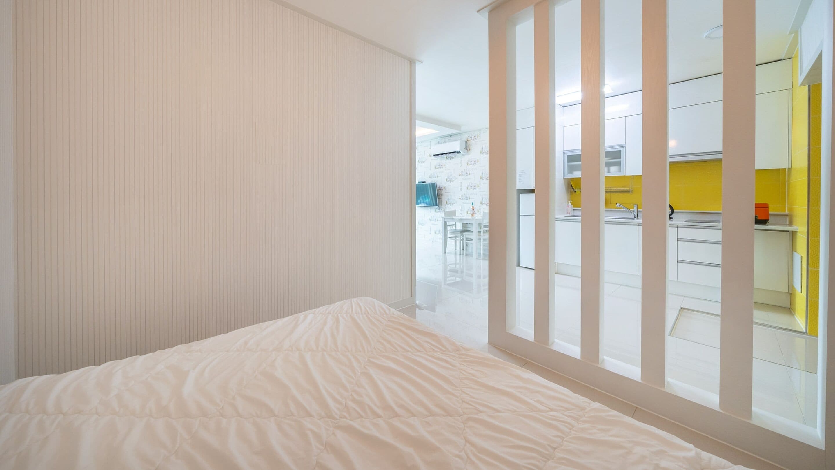 A bedroom with a bed, a sliding door leading to a kitchen, and a view of the kitchen area.