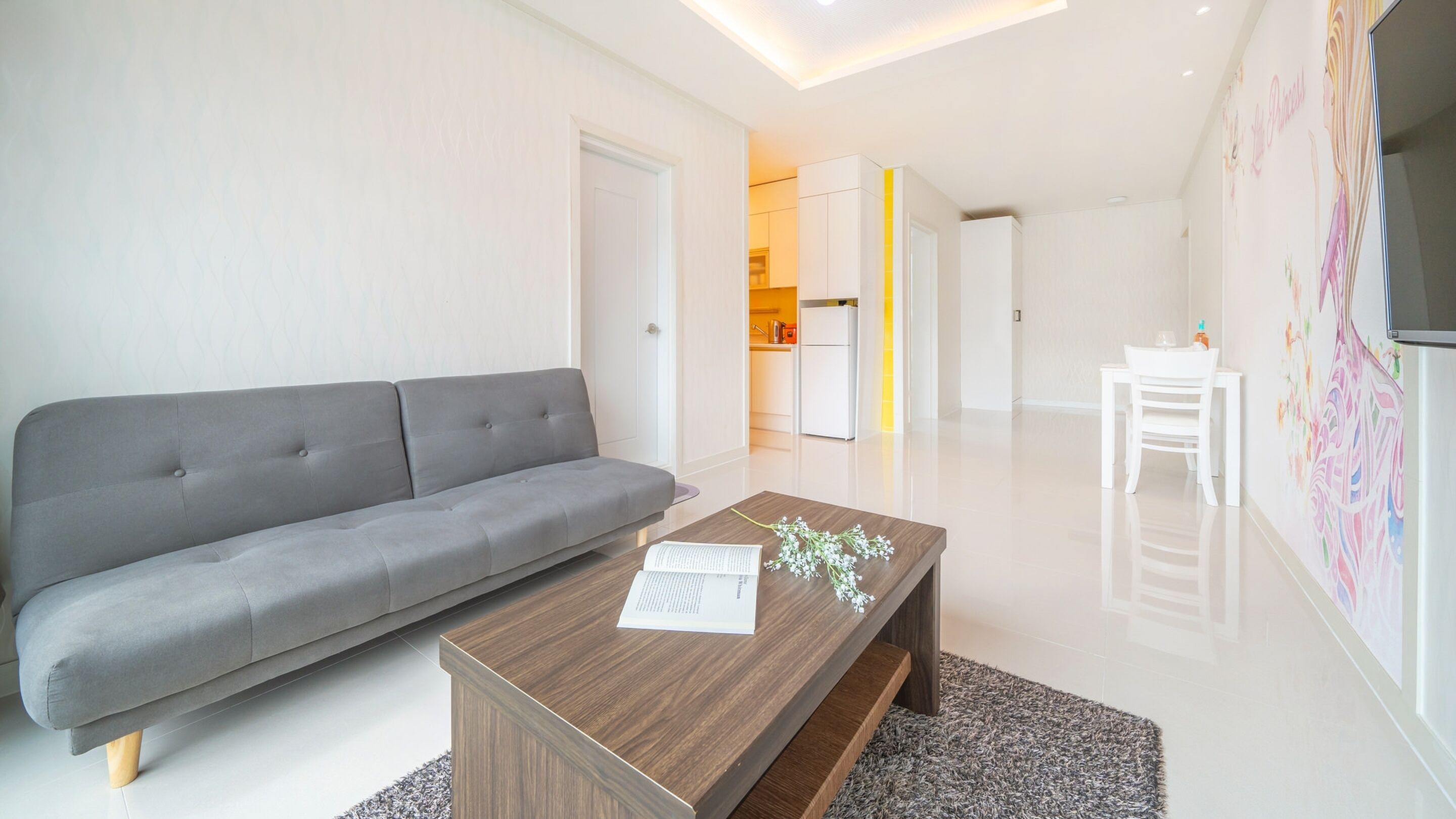 A modern living room with a grey sofa, a wooden coffee table, and a white dining table.