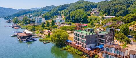 Un pueblo a orillas del río, con edificios a lo largo de la orilla, un muelle con barcos y un puente que une las zonas.