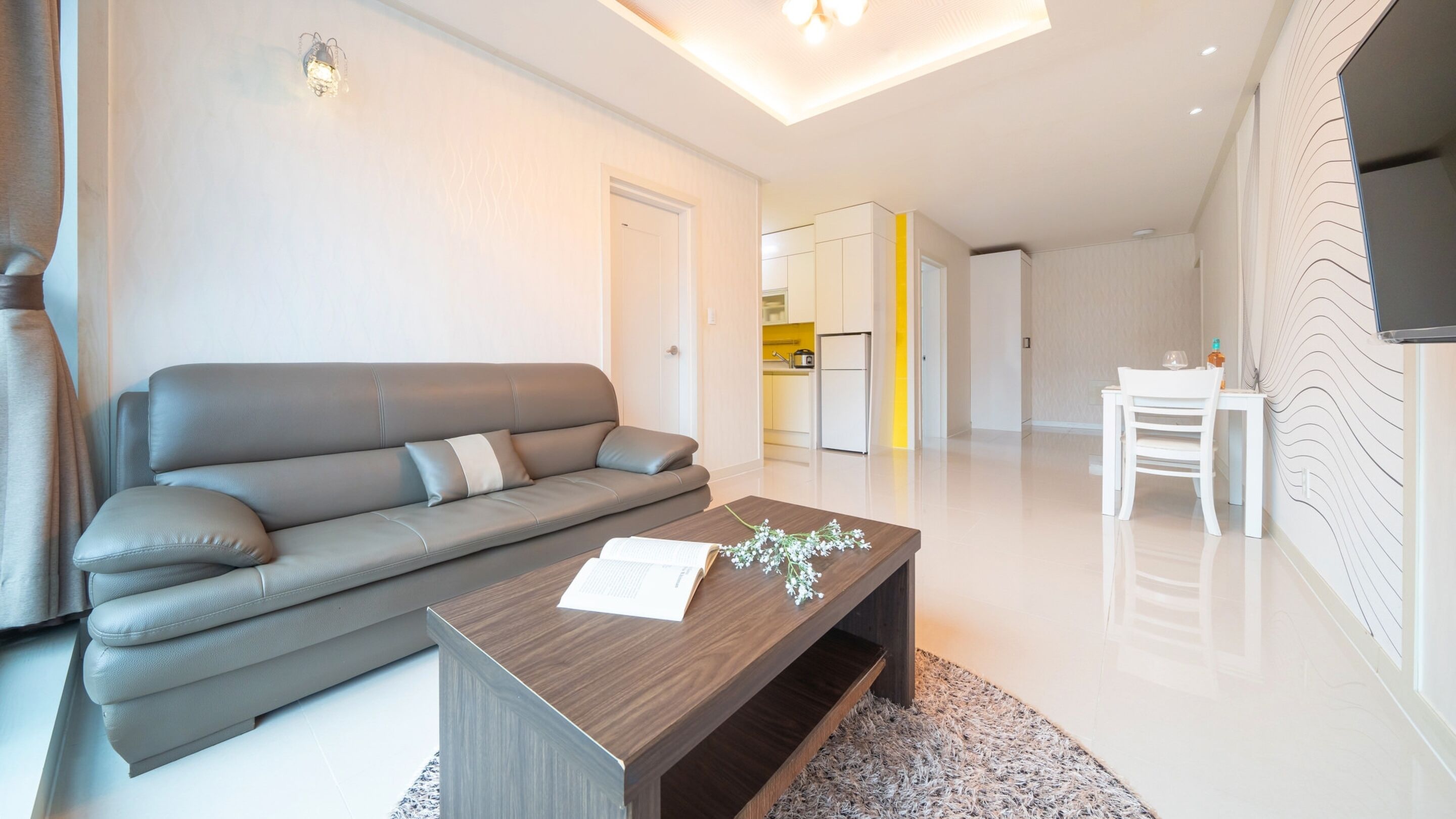 A modern living room with a grey sofa, a wooden coffee table, and a TV mounted on the wall.