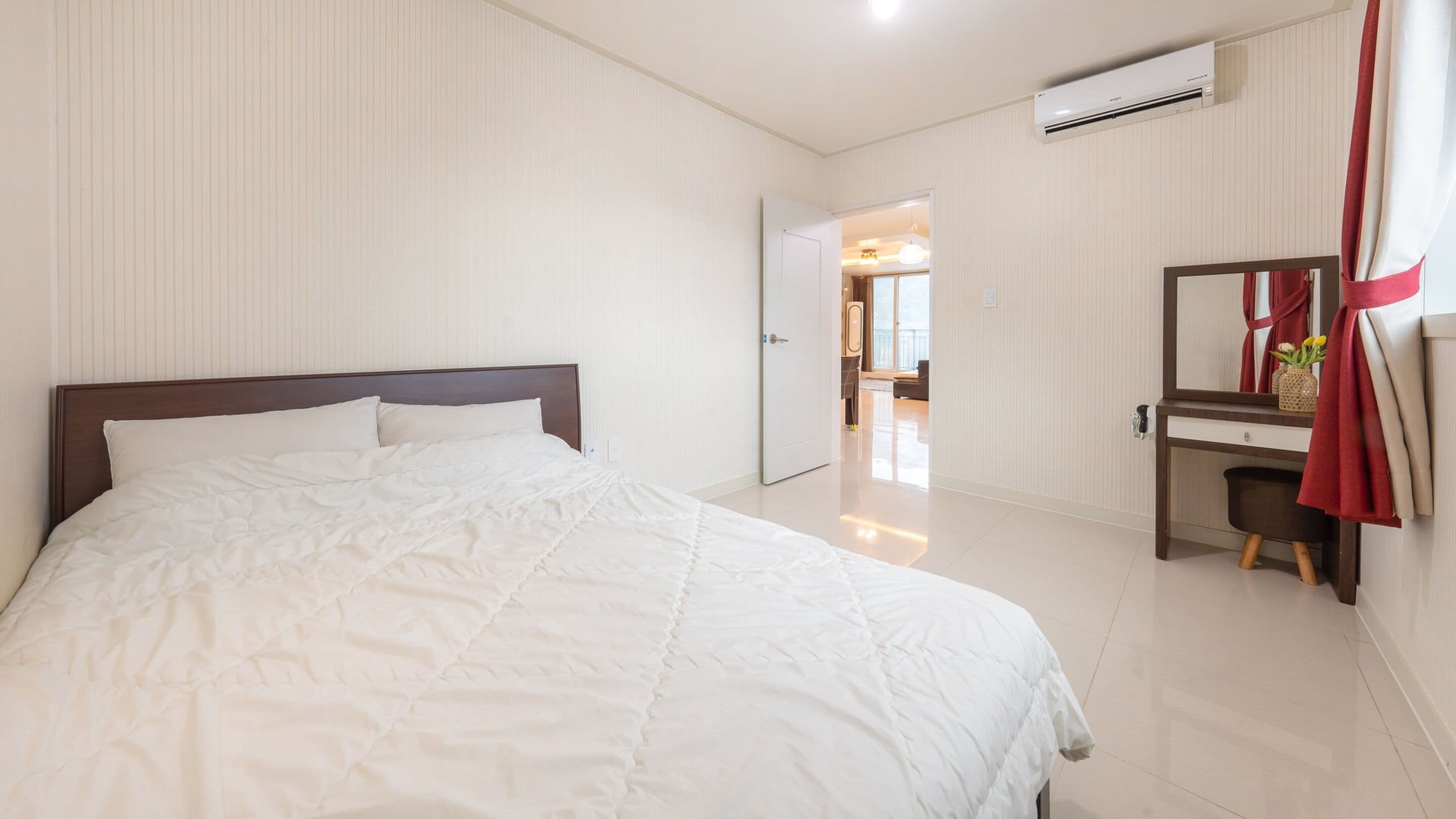 A hotel room with a large bed, a desk with a mirror, and an air conditioning unit on the wall.