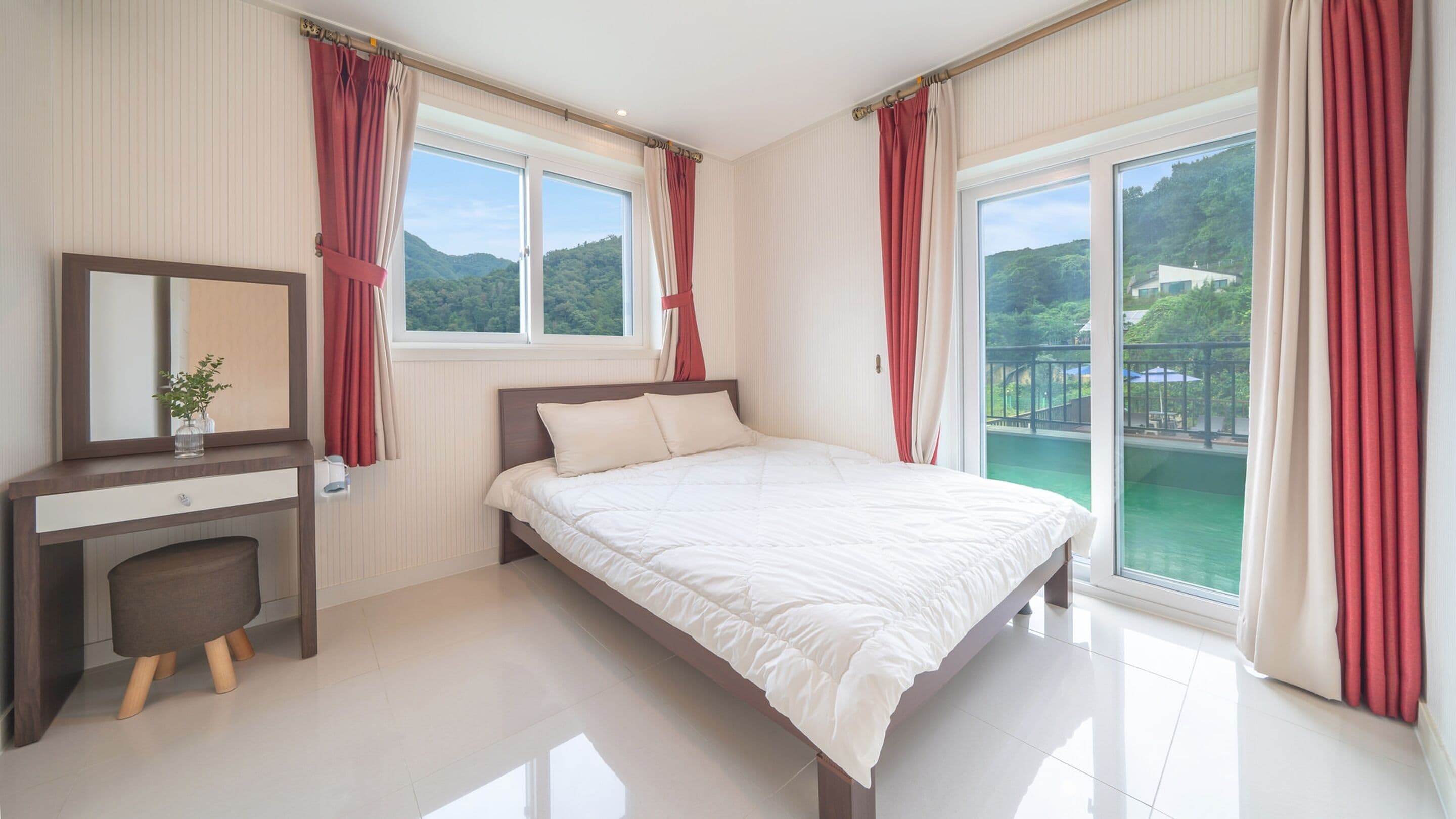 A modern bedroom with a large bed, a bedside table with a mirror, and a view of a green landscape through the window.