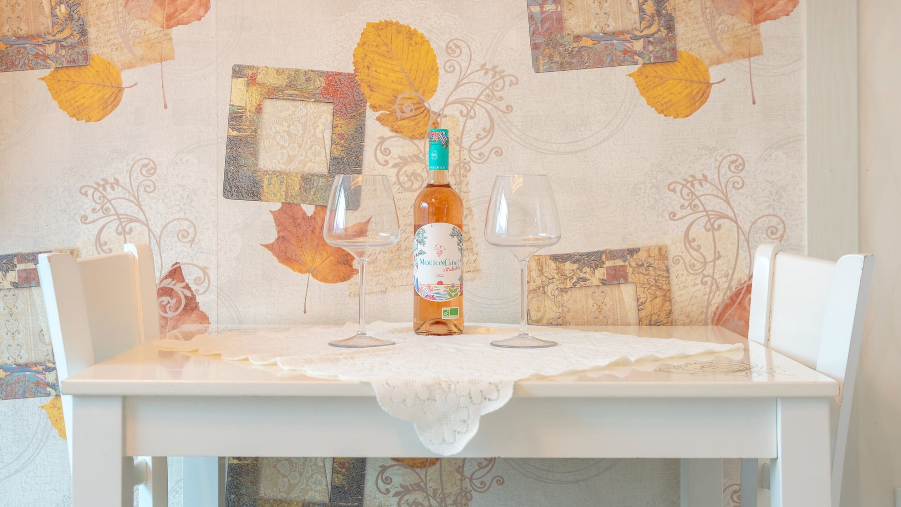 A table with a bottle of Mouton Cadet wine and two empty wine glasses, set on a table with a lace tablecloth.