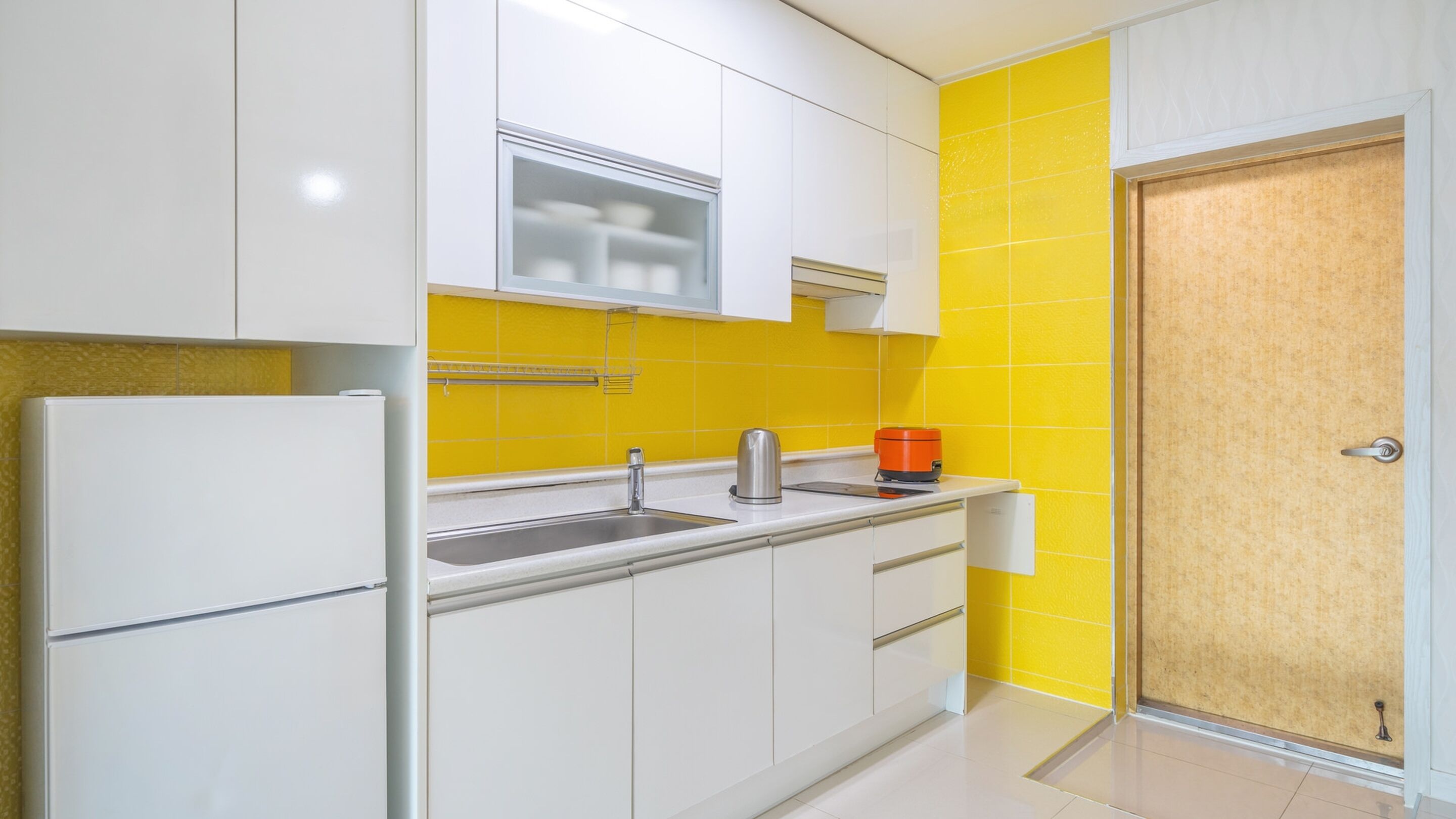 A compact kitchen with white cabinets, a stainless steel sink, and a yellow backsplash.