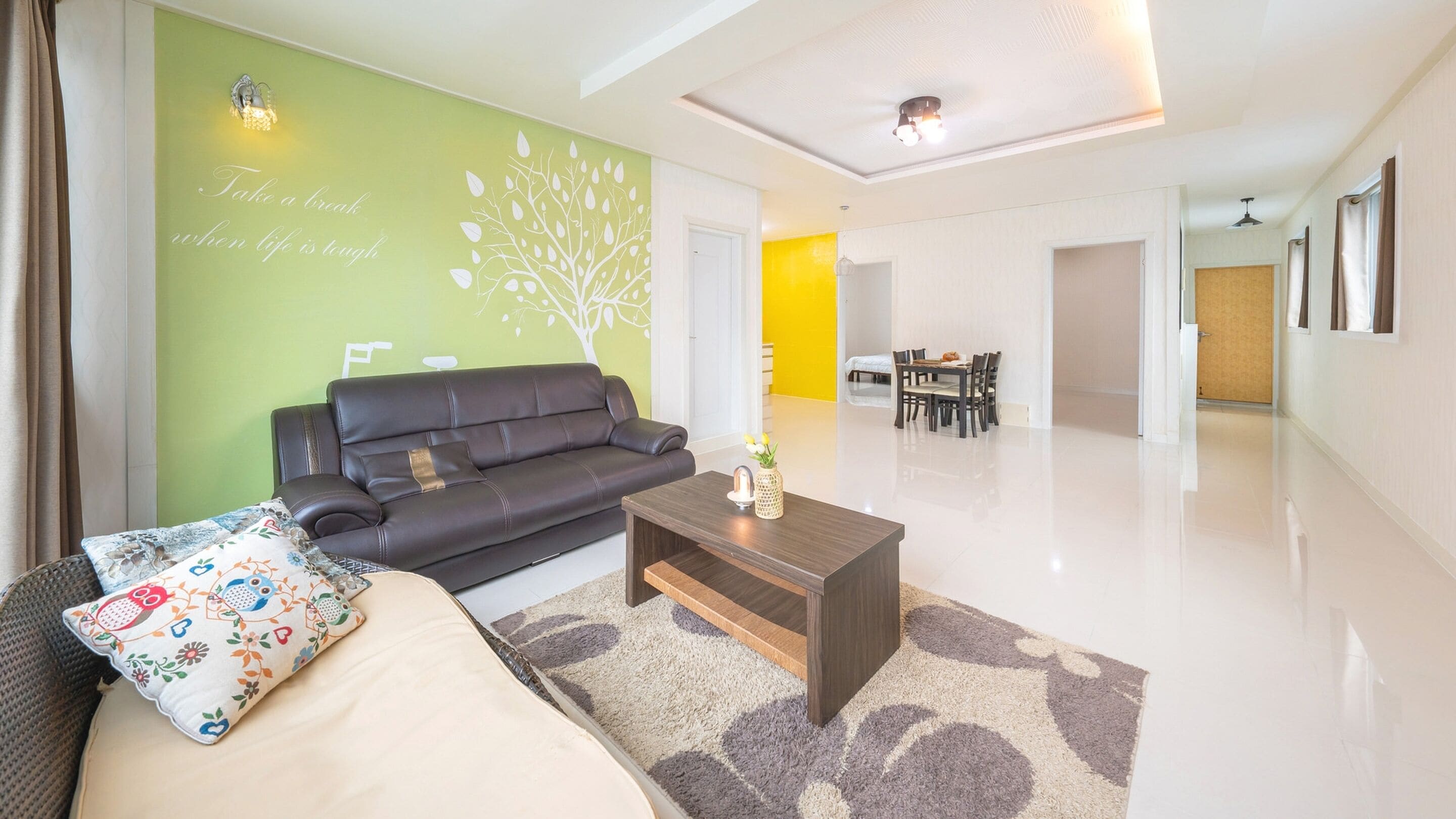A modern living room with a sofa, coffee table, and a green accent wall with a tree design.
