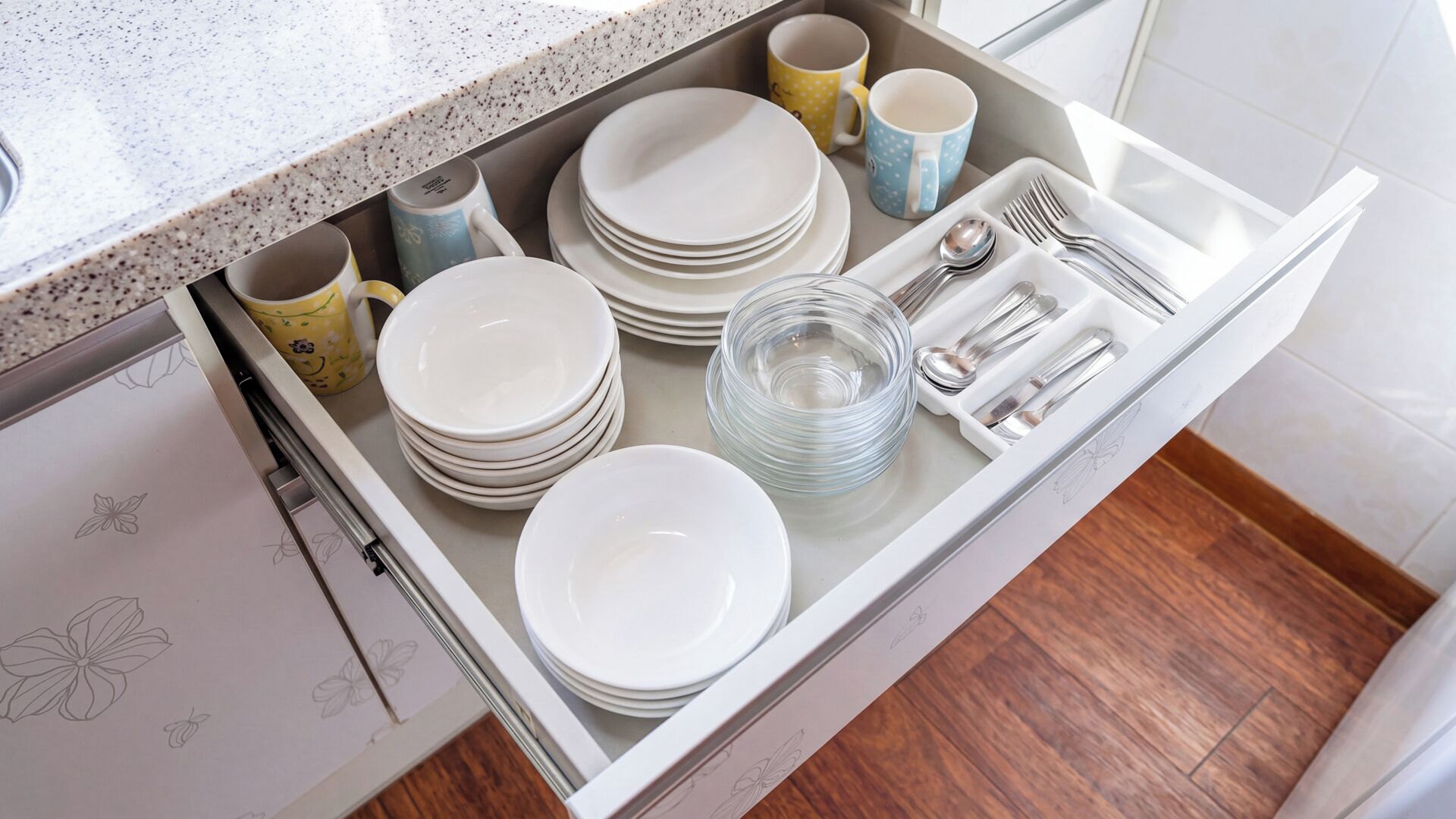 A kitchen drawer with stacked white plates, clear glassware, and utensils.