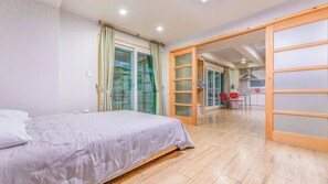 Une chambre avec un lit, une porte-fenêtre coulissante donnant sur un coin repas et une cuisine visible à travers la porte.