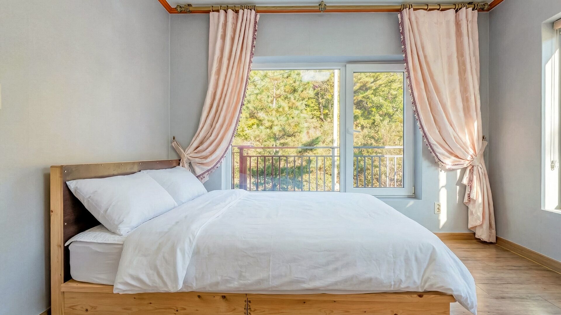 A bedroom with a wooden bed, white bedding, and a balcony with curtains.
