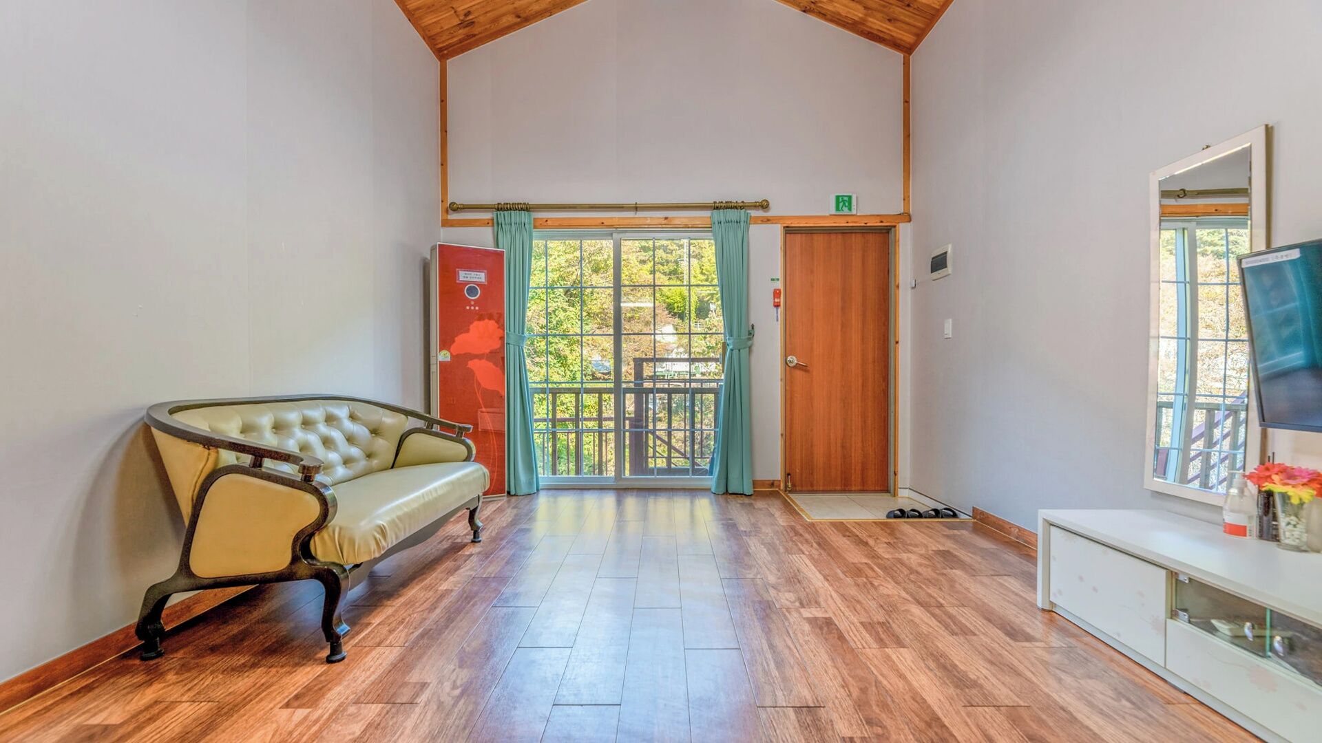 A room with a wooden ceiling, a sofa, a television, and a door leading to an outdoor area.