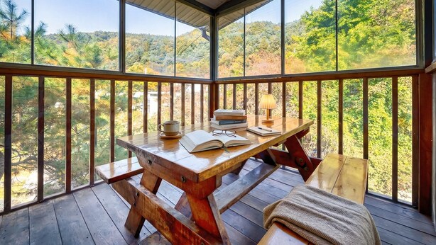 Una terraza de madera con una mesa, un banco, libros, una taza y una lámpara.
