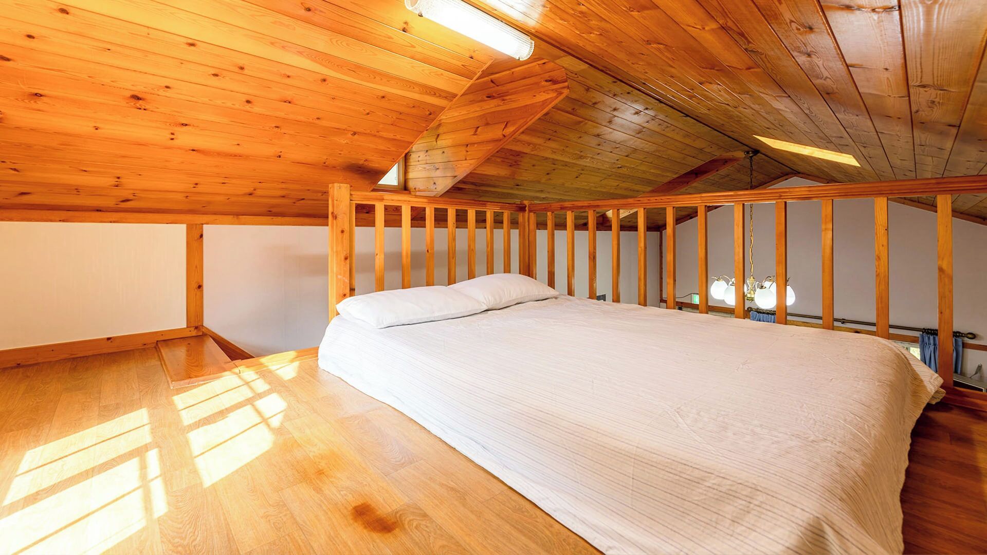 Een kamer met een houten plafond, een bed met wit beddengoed en een houten vloer.