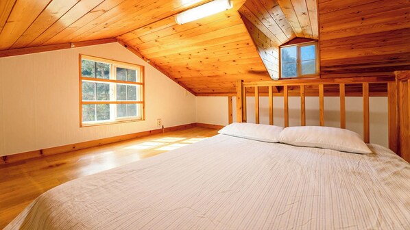Un dormitorio con techo inclinado, un ventanal grande y una cama con almohadas.