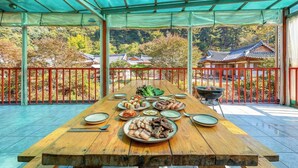 Una mesa de madera dispuesta para una comida, con diversos platos, una parrilla y vistas a edificios tradicionales.