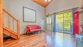 A room with a wooden staircase, a red sofa, a large window with a view of greenery, and a door with a red sign.