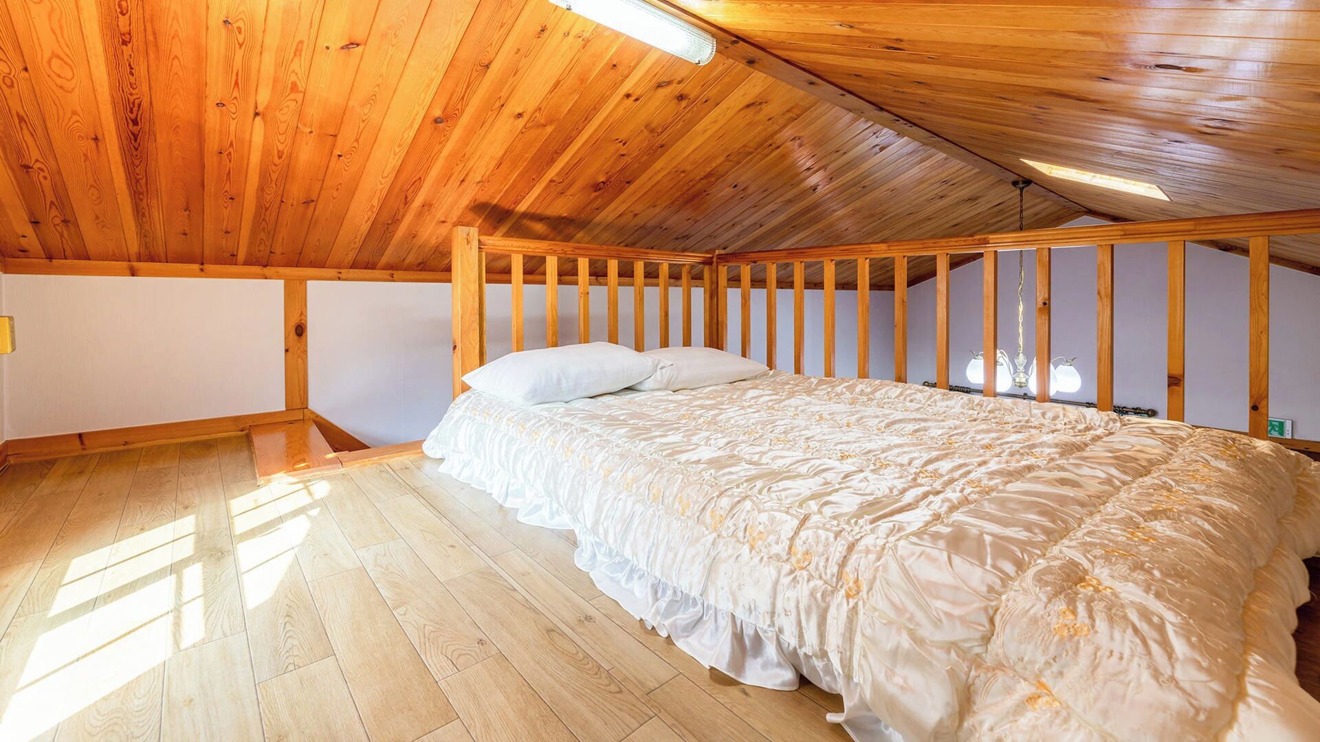 Un dormitorio con techo de madera, cama con ropa de cama blanca y suelo de madera.
