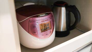 A pink electric rice cooker with a digital display, placed next to a stainless steel electric kettle on a shelf.