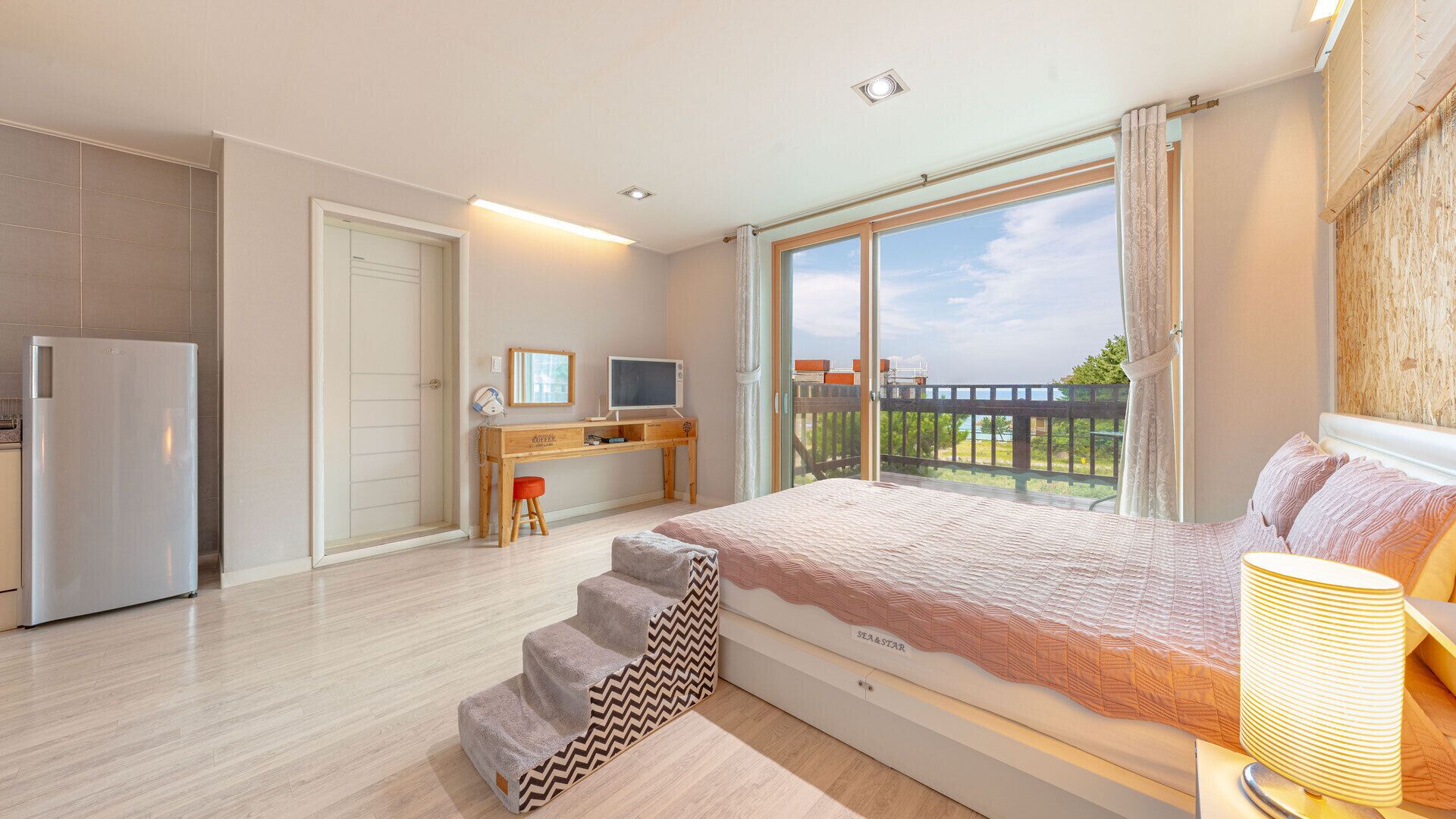 A bedroom with a bed, a desk, a television, and a view of the outdoors.