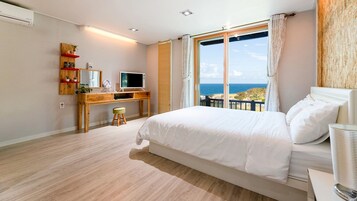 Un dormitorio con una cama grande, un escritorio con computadora y vistas al mar.
