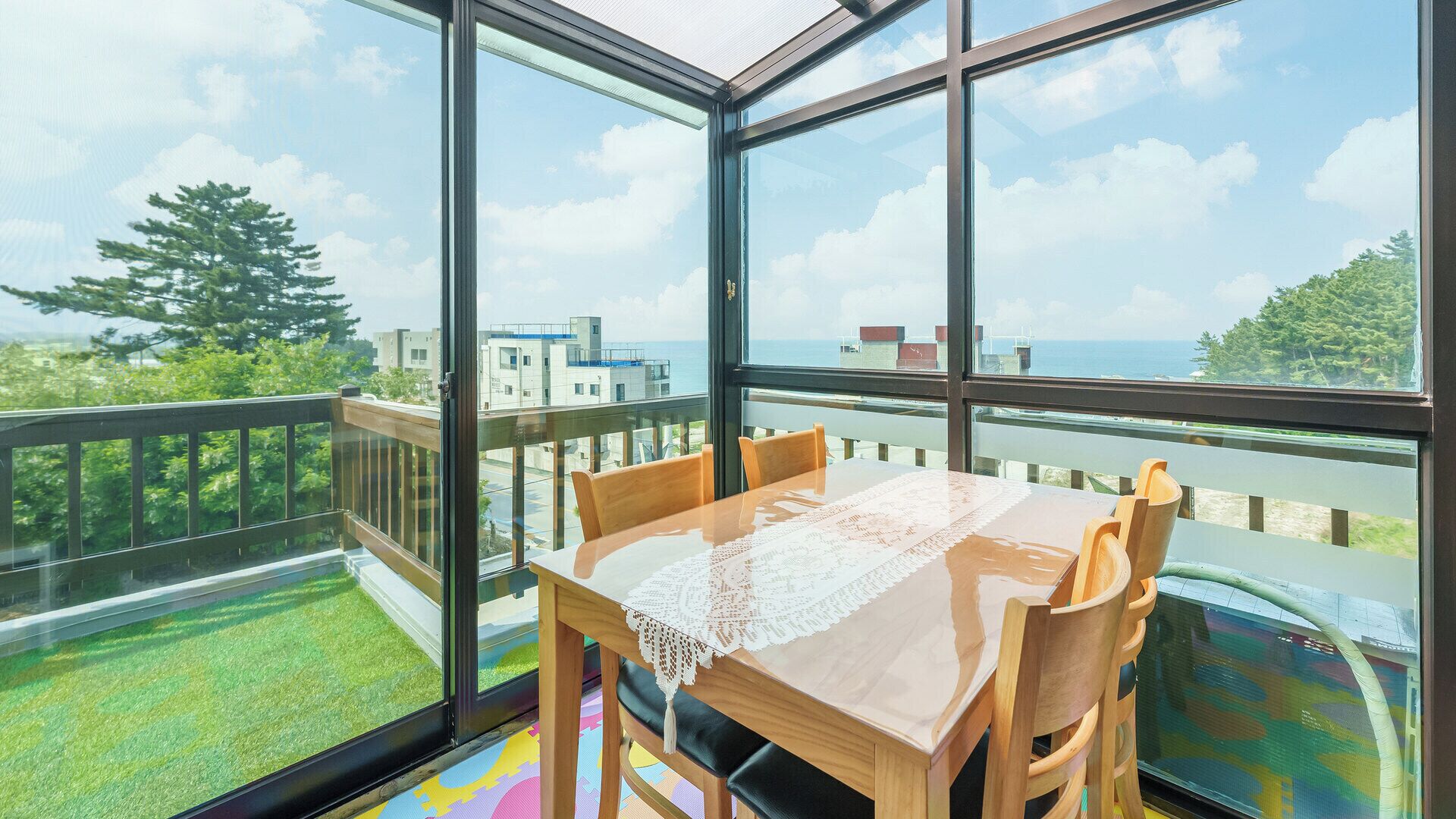 Un comedor con una mesa y sillas, ventanas amplias y vistas al mar y edificios.
