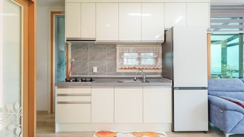 A modern kitchen with white cabinets, a stainless steel refrigerator, and a window with lace curtains.