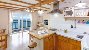 A kitchen with wooden cabinets, a central island, and a view to the sea through a sliding door. - Ganghwa Hana & Alice spa Pension (Incheon)