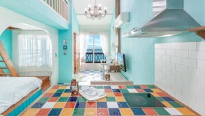 A room with a colorful checkered floor, a bed, a chandelier, and a view of the sea through a window. - Ganghwa Hana & Alice spa Pension (Incheon)