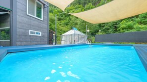 A swimming pool with a clear blue water, surrounded by a grey building and a green landscape. - Gapyeong Myeonyeokgongbang Private Villa (Gapyeong)