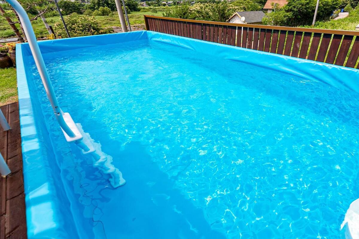 A rectangular above-ground pool with a wooden deck and a ladder.