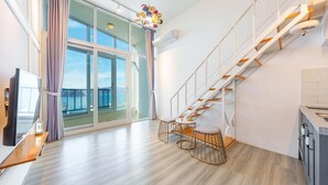 Uma sala de estar moderna com uma grande porta de vidro deslizante para uma varanda, uma escada de madeira e uma pequena mesa redonda com uma cadeira.