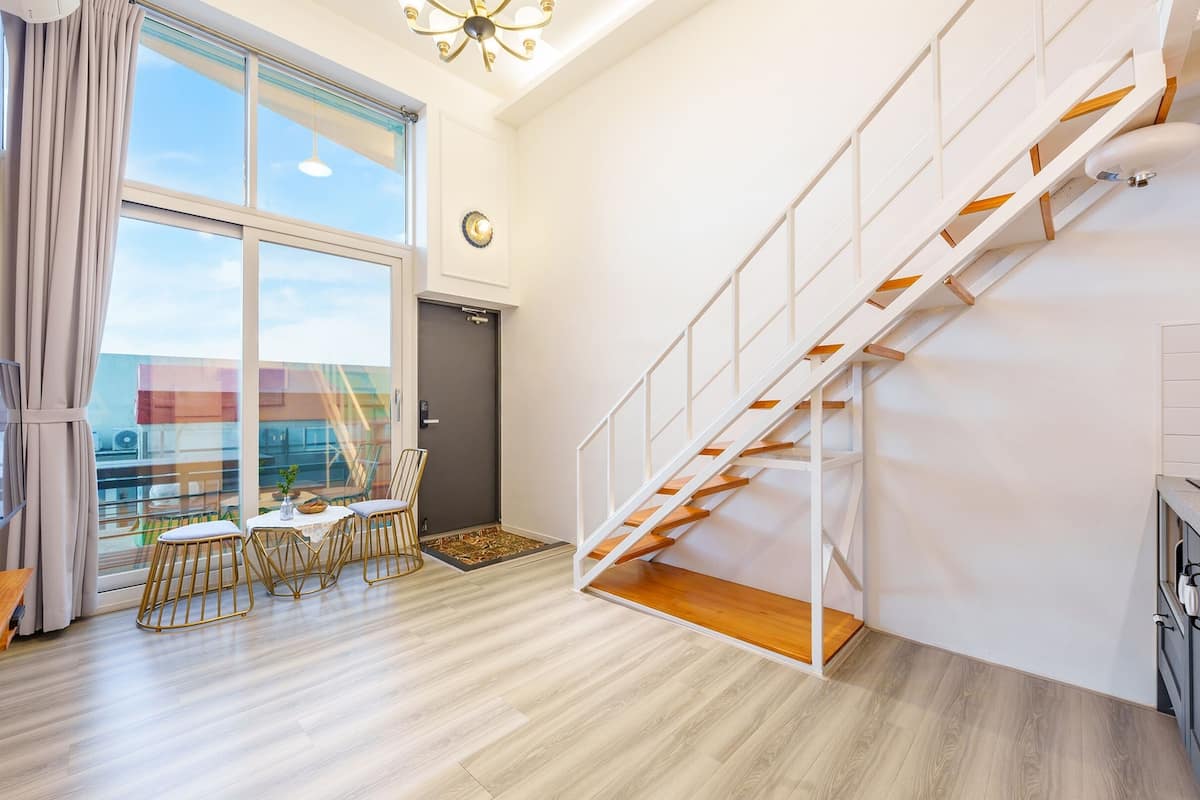 A modern apartment with a large window, a dining area, a staircase, and a kitchen.