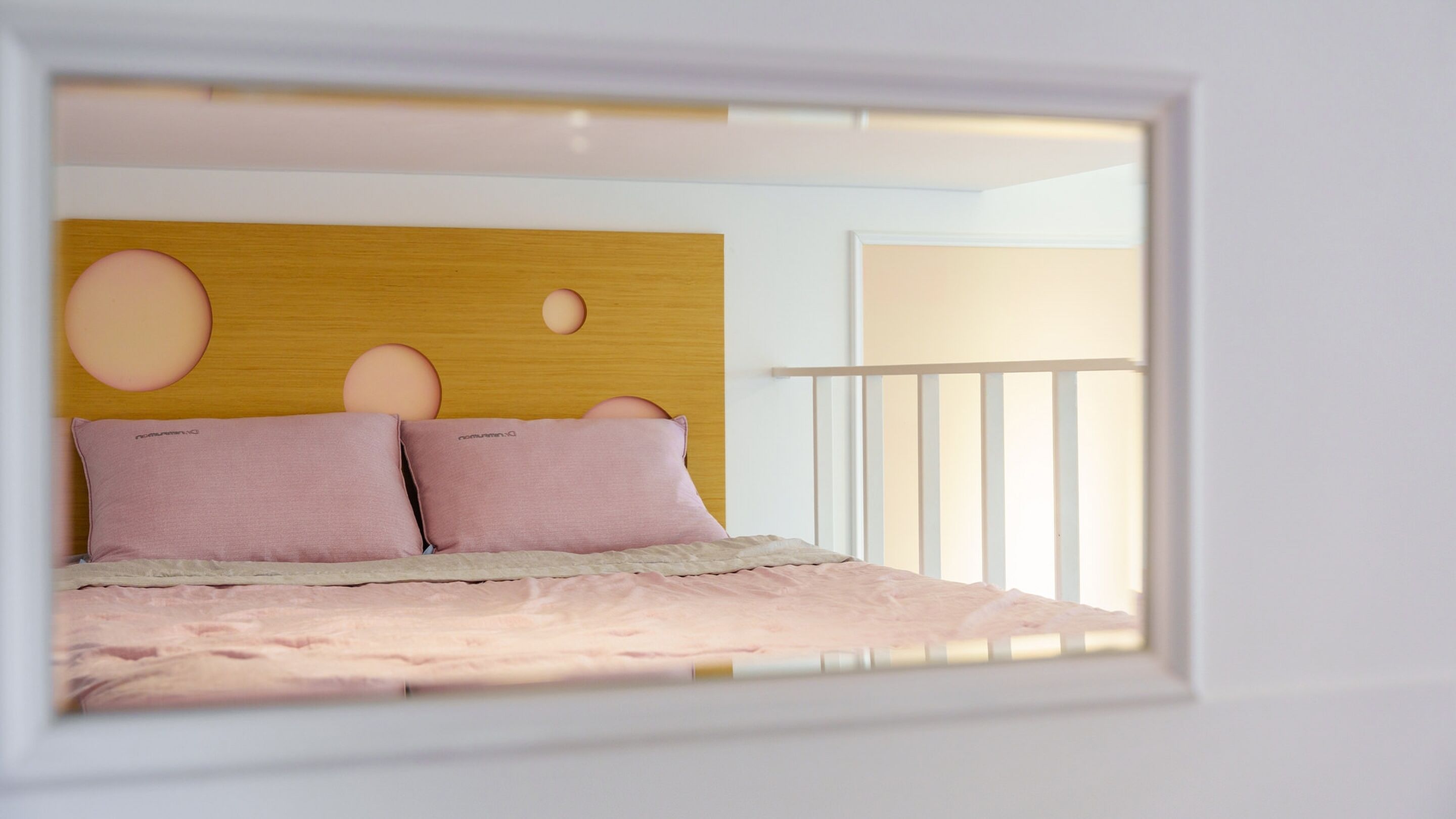 Quarto com cabeceira de madeira, duas almofadas cor-de-rosa e guarda-corpo branco.