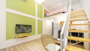 A modern apartment with a loft bedroom, a dining area with a TV, and a staircase.