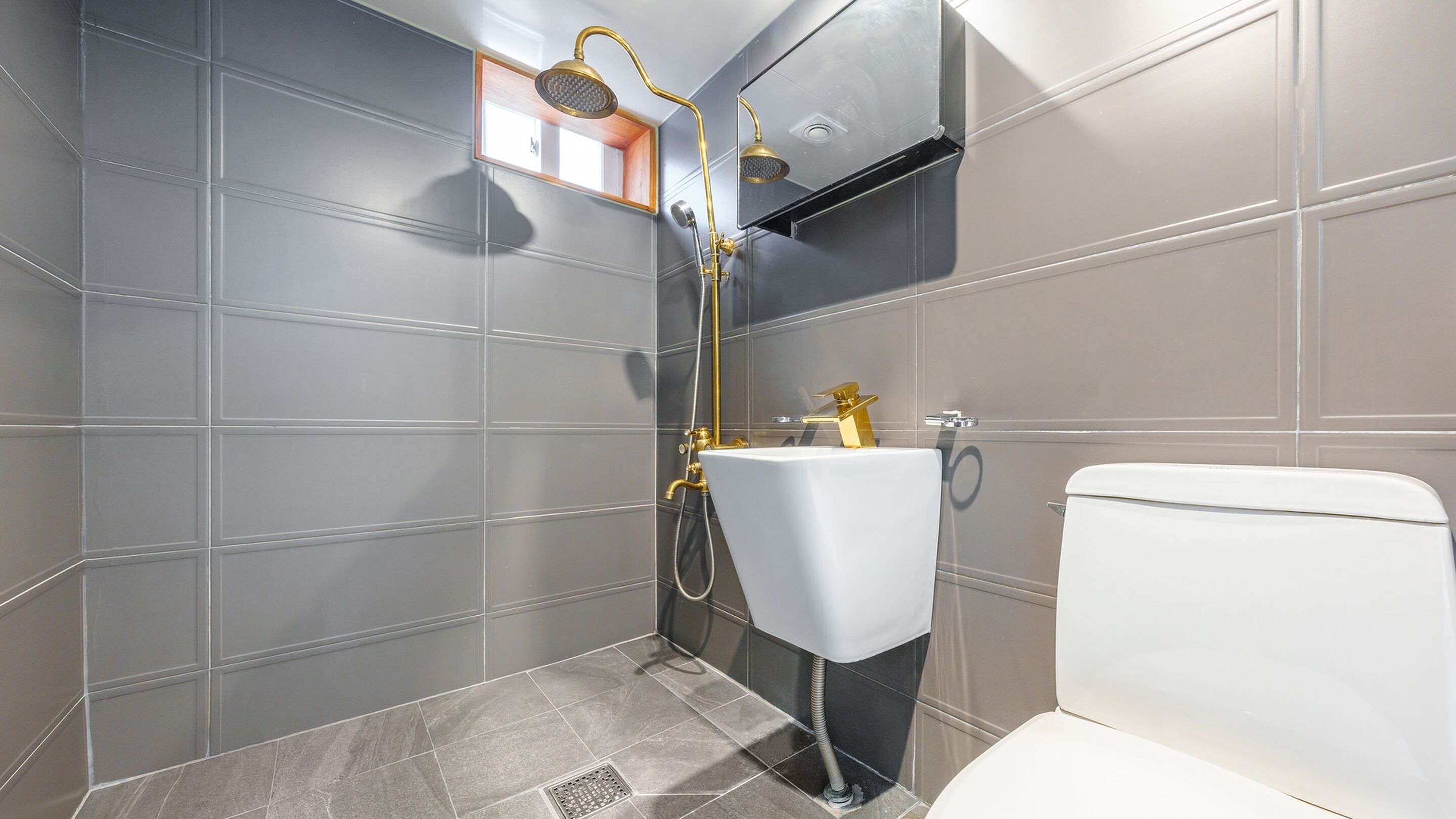 A modern bathroom with grey tiles, a white sink, and a toilet.
