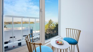 Uma varanda com vista para um corpo de água e terra ao longe, mobiliada com uma cadeira e uma pequena mesa.