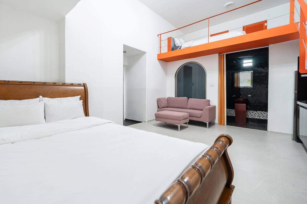 A hotel room with a large bed, a pink armchair, and a balcony with orange railings.