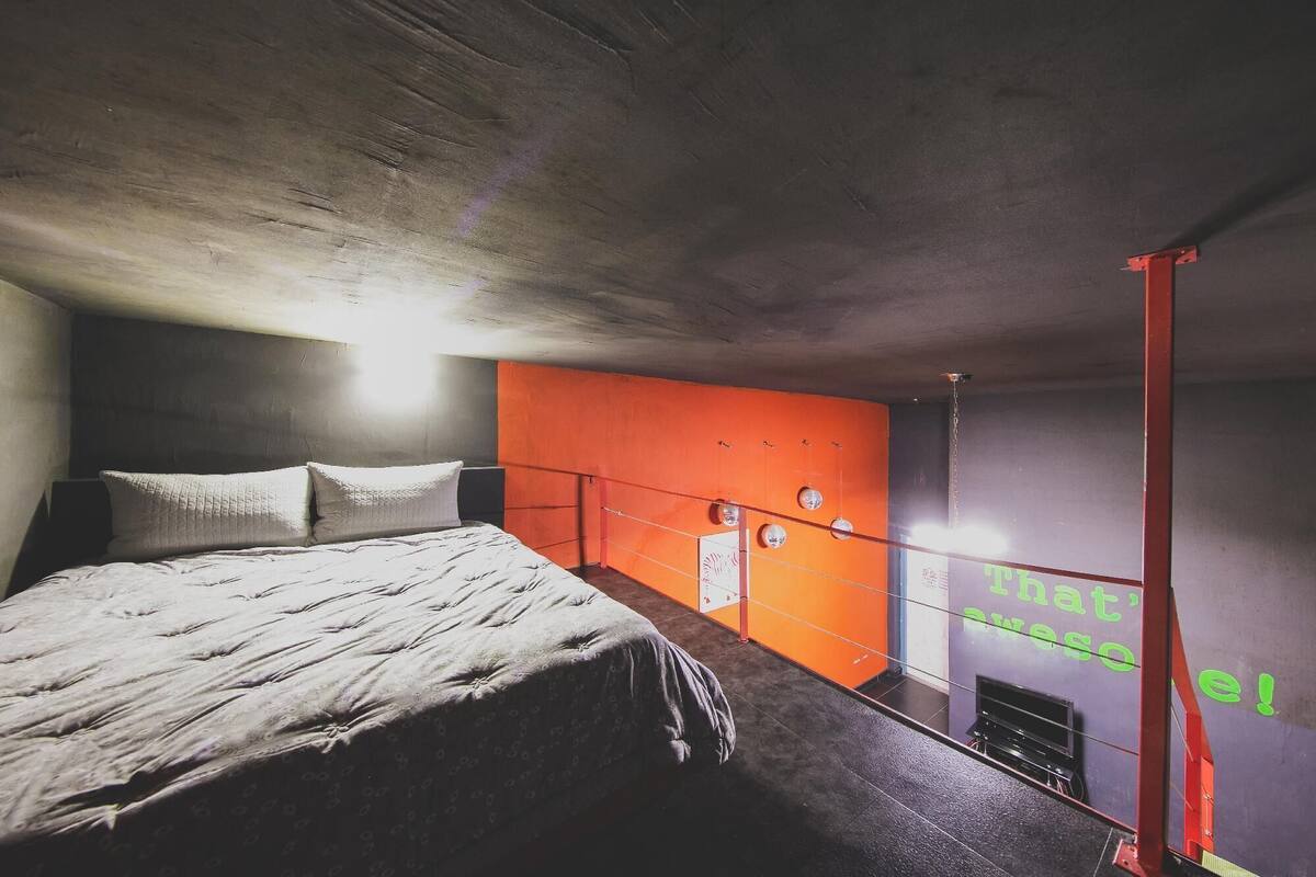 A bedroom with a bed, a red wall, and a window with a view.