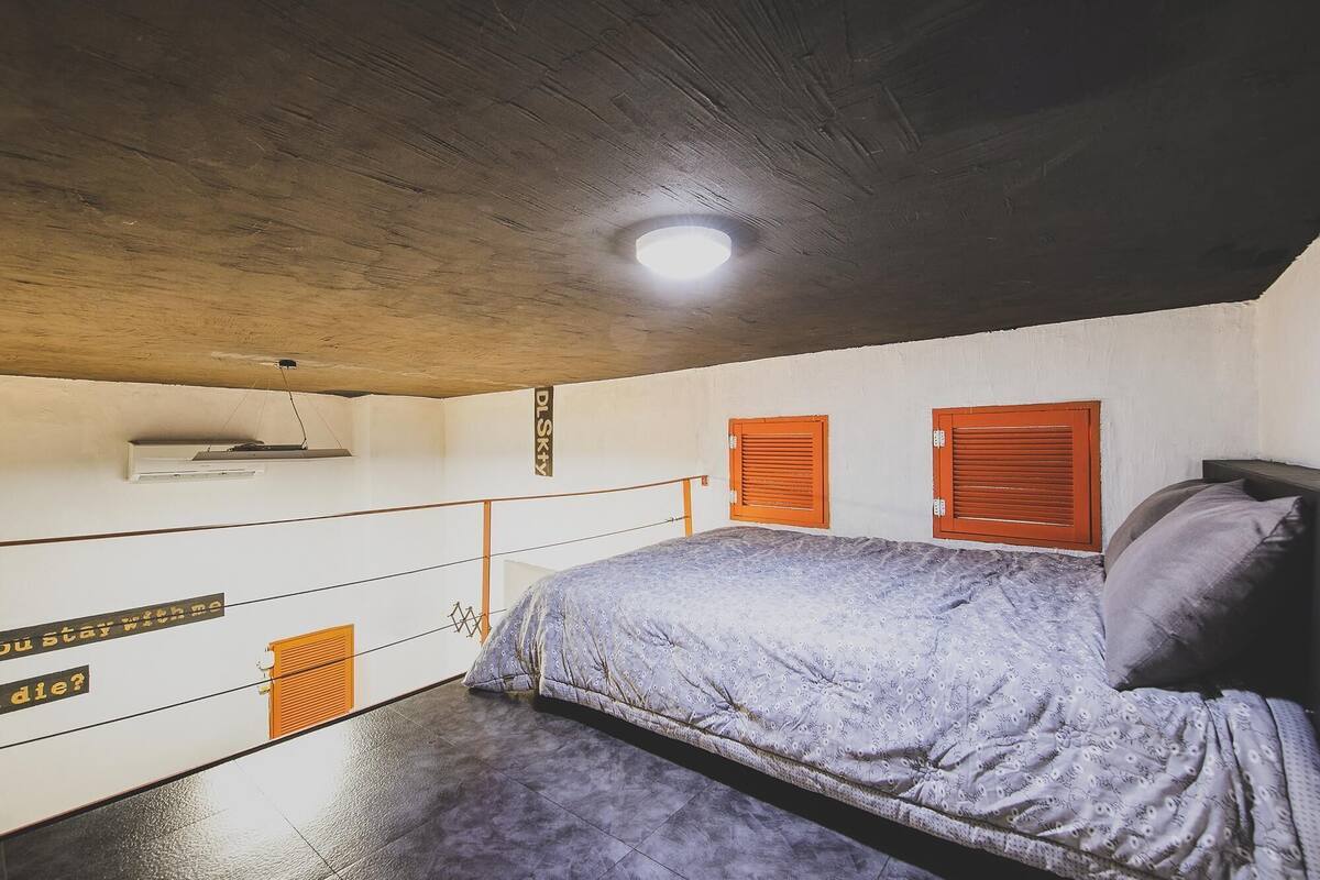 A bedroom with a bed, a ceiling light, a window with shutters, and a wall-mounted air conditioning unit.