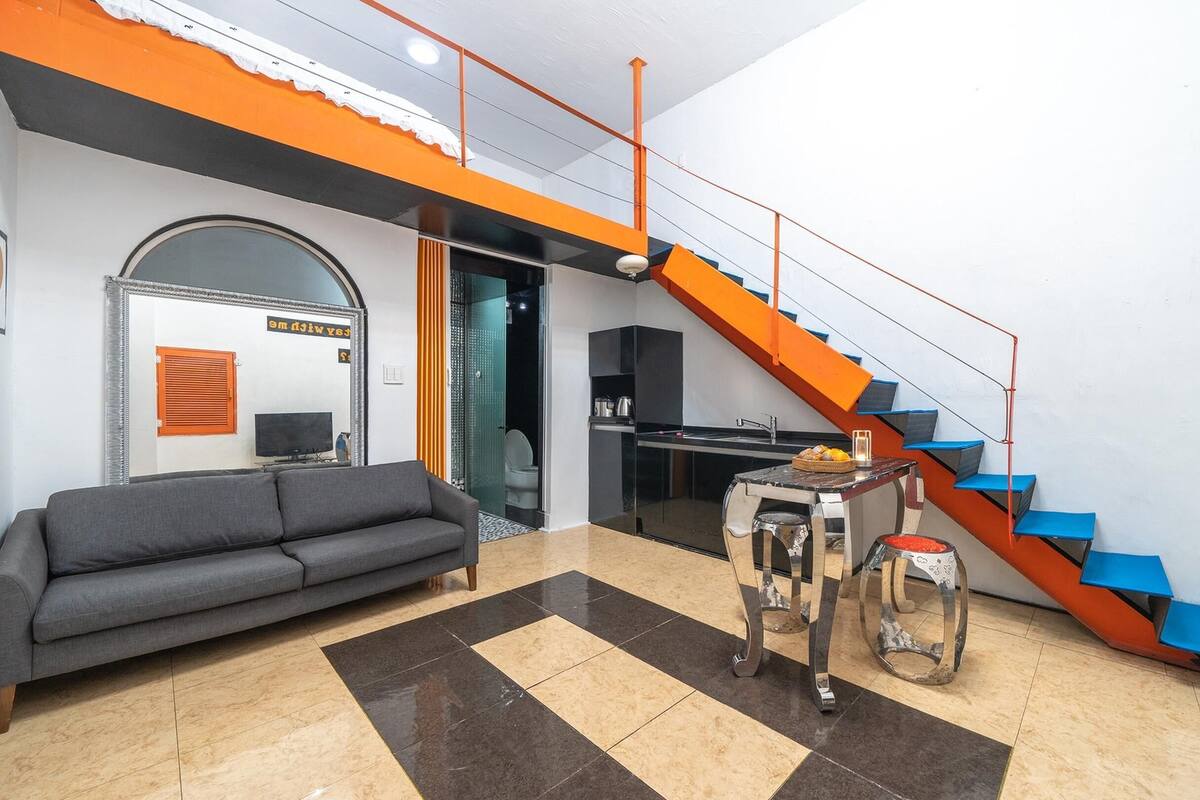 A modern living room with a sofa, a dining table, and a kitchen area with a staircase.