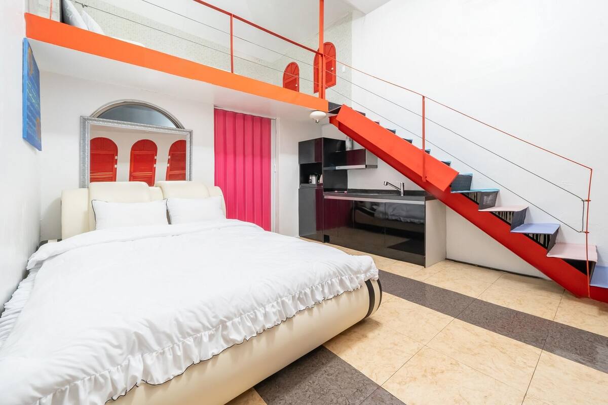 A modern hotel room with a bed, a staircase, and a kitchenette.