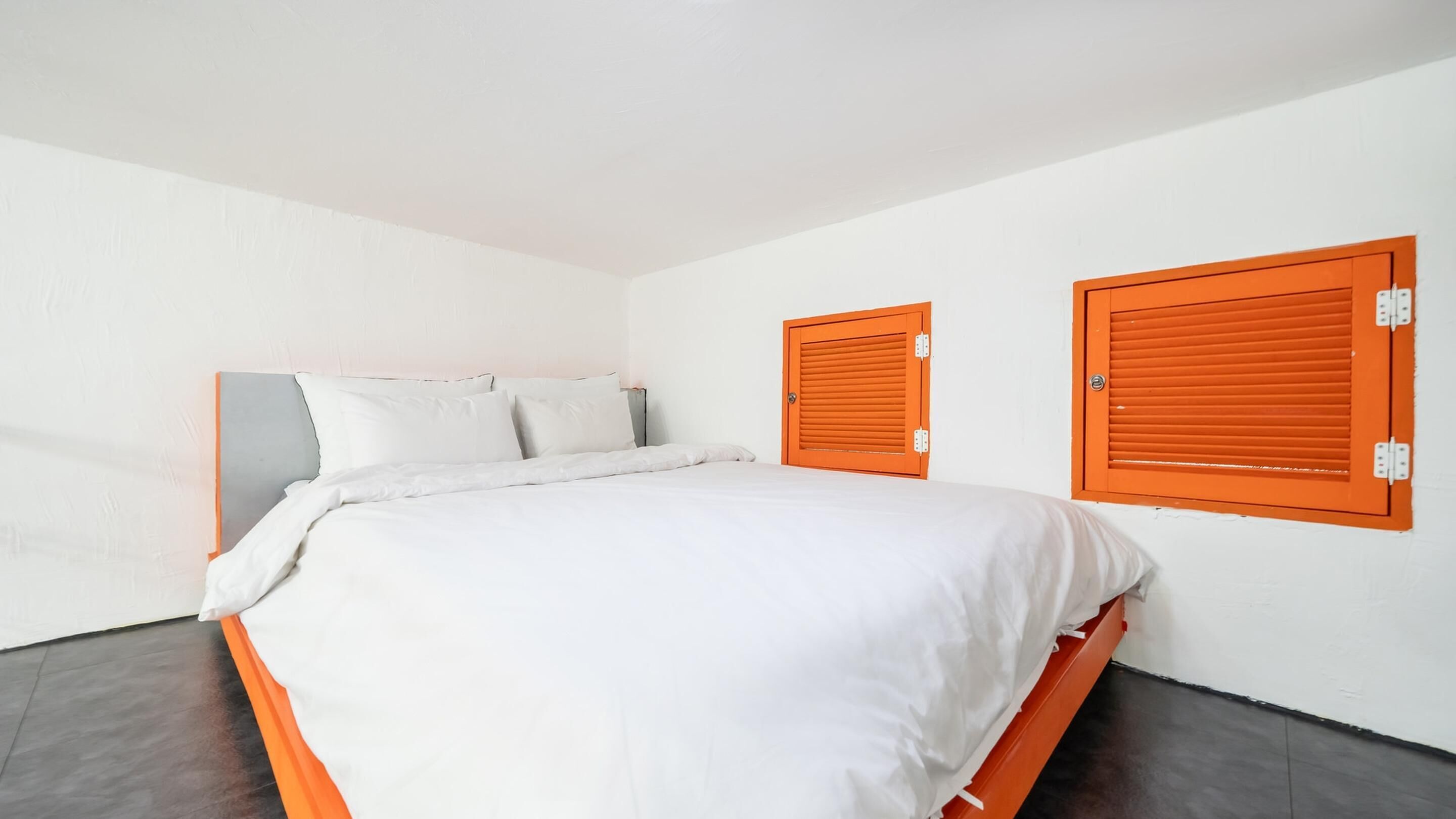 A modern bedroom with a large bed, white bedding, and two orange shutters on the walls.